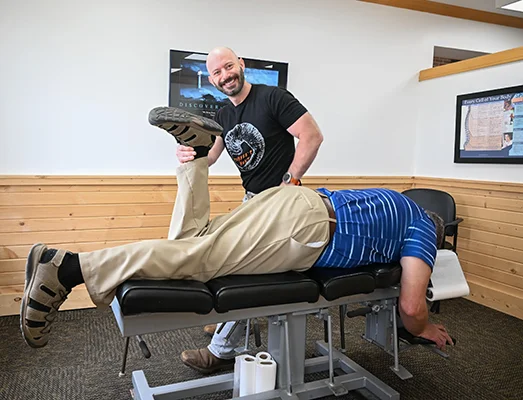 Dr. Matt Pamer smiling at the camera and raising a patient's leg during an adjustment